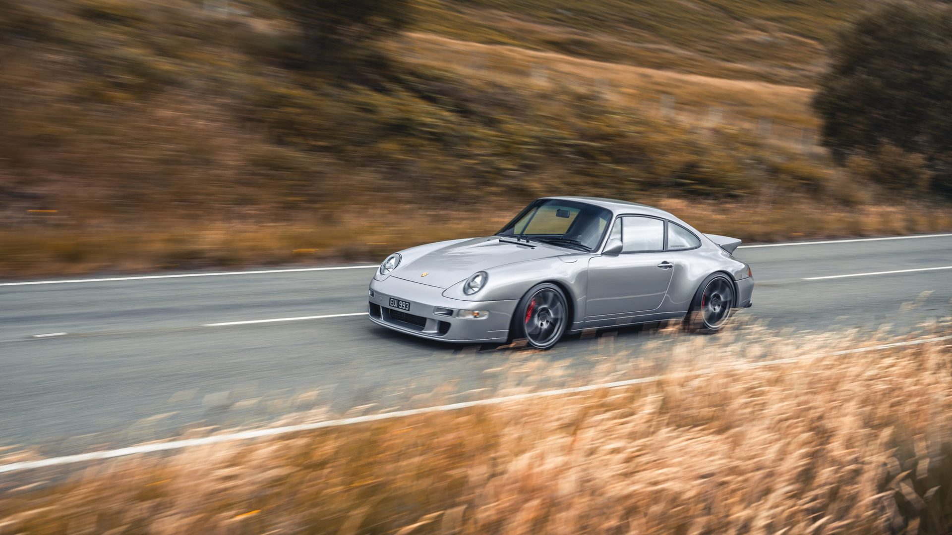 A silver air-cooled 911 at speed on an open road.